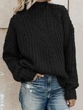 Black chunky knit mock neck sweater with a central cable-like texture, relaxed fit, and long sleeves styled with distressed blue jeans.