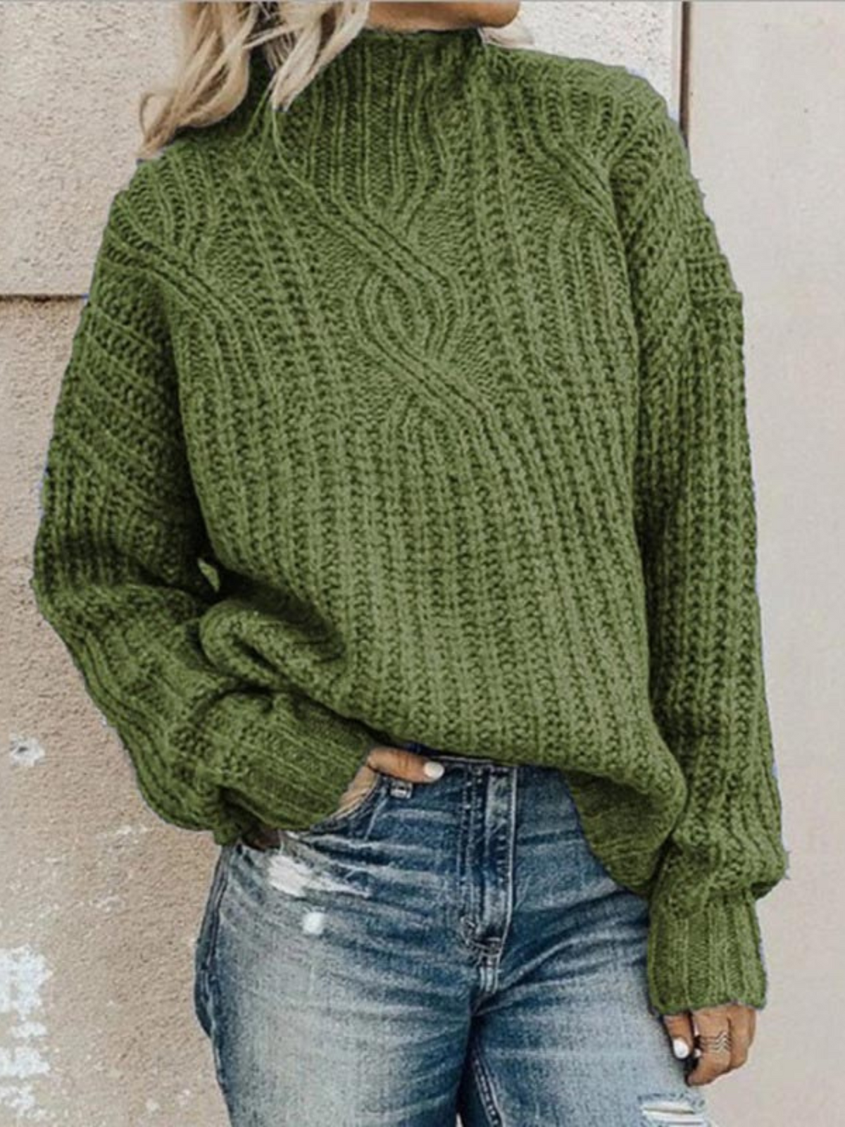Olive green chunky knit mock neck sweater featuring vertical ribbing and a central textured cable pattern above blue jeans.