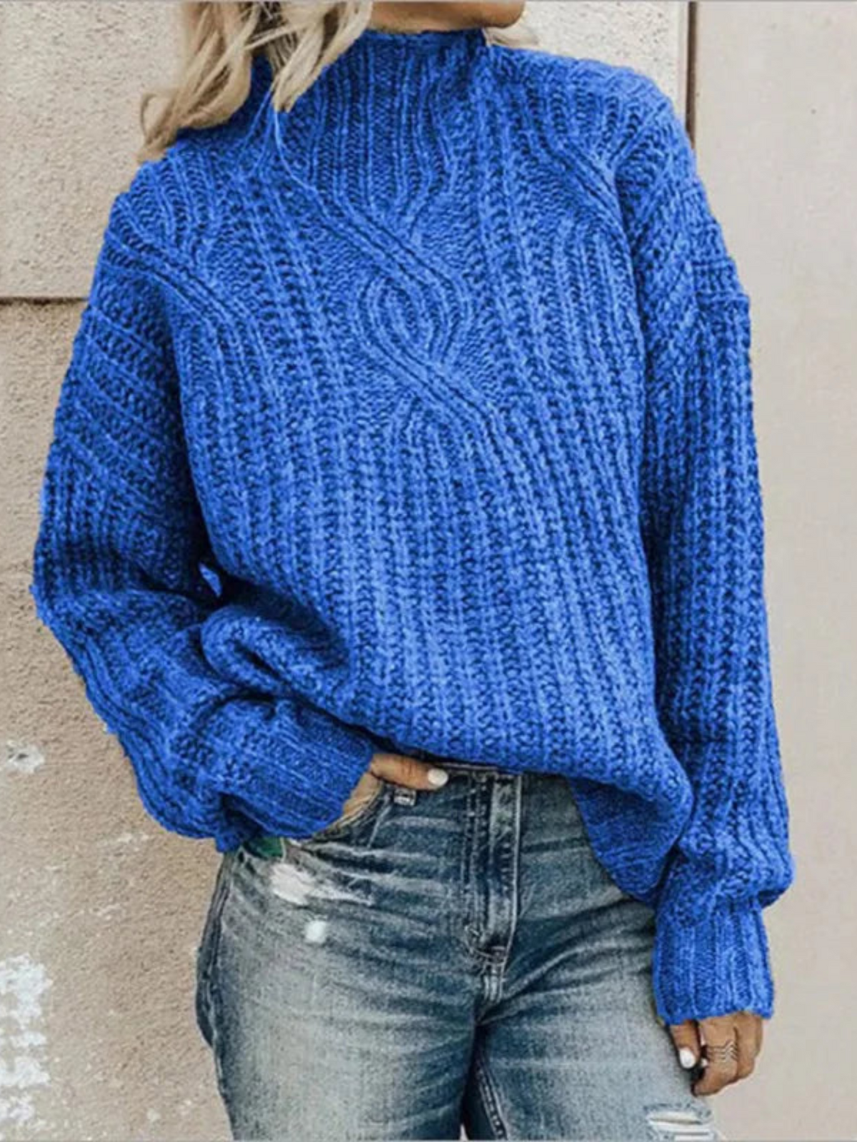 Bright blue chunky knit mock neck sweater showing its raised central pattern and ribbed texture with faded jeans.