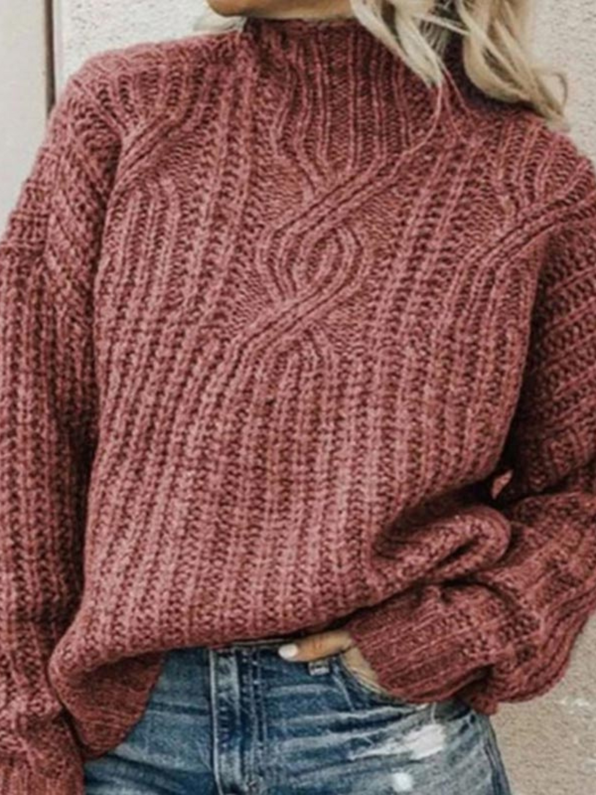 Dusty rose chunky knit mock neck sweater with a prominent center cable design and sleeves gathered near the waist over blue jeans.