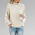 Cream chunky knit turtleneck sweater featuring a generous ribbed neckline and oversized sleeves, paired with distressed jeans.