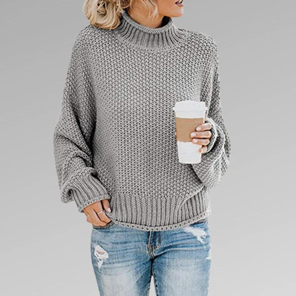 Gray chunky knit turtleneck sweater with a relaxed silhouette and structured ribbed trim, styled with distressed denim.