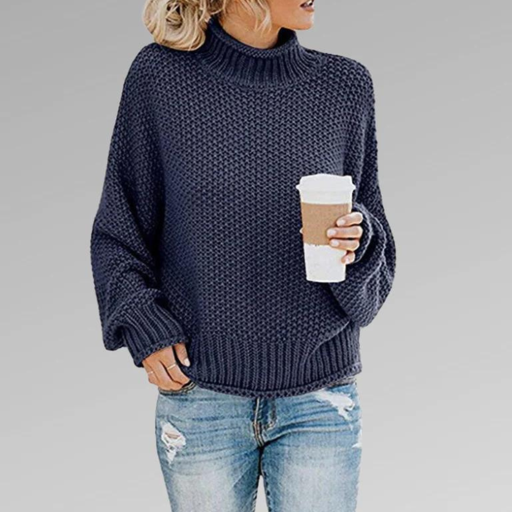 Navy chunky knit turtleneck sweater with dropped sleeves and ribbed edges, worn with distressed jeans.