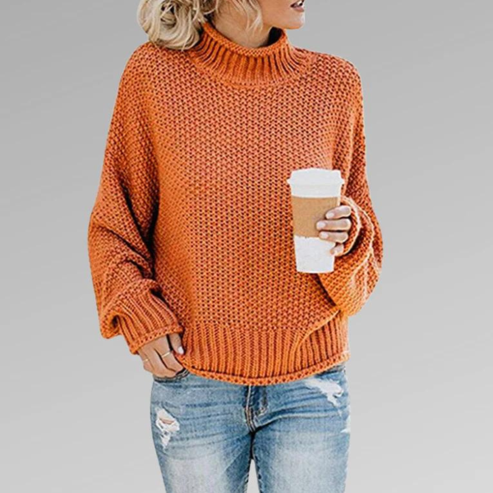 Orange chunky knit turtleneck sweater with wide sleeves and ribbed cuffs, styled with distressed blue jeans.