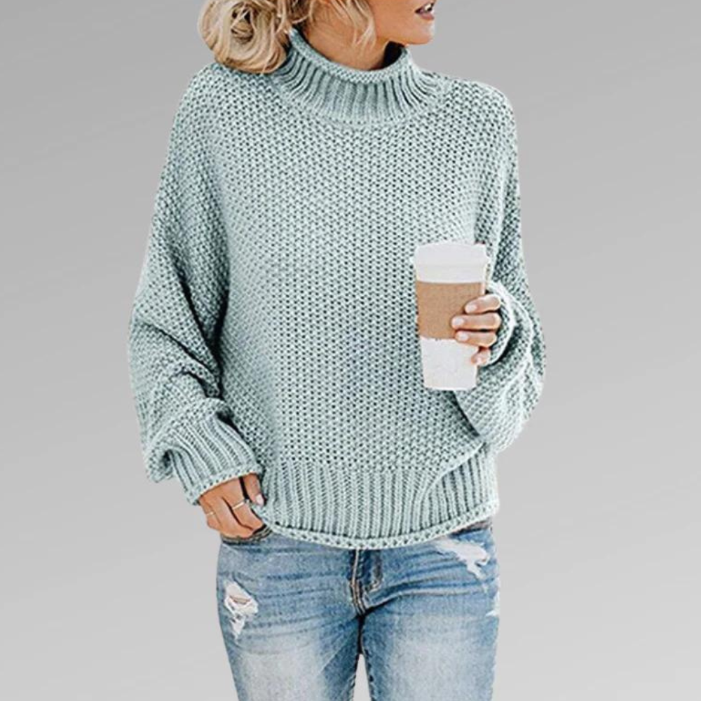 Light blue chunky knit turtleneck sweater with an oversized ribbed collar and cuffs, shown with distressed jeans and a coffee cup.