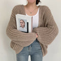 Taupe chunky open-front cardigan styled over a white top and jeans, with oversized balloon sleeves gathered across the front.