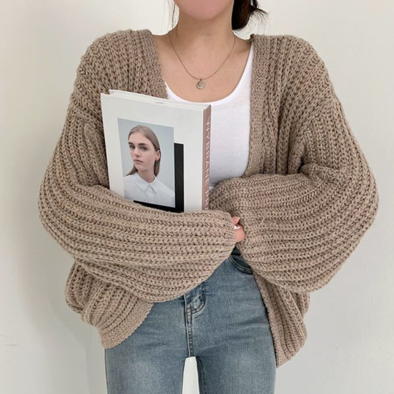 Taupe chunky open-front cardigan styled over a white top and jeans, with oversized balloon sleeves gathered across the front.