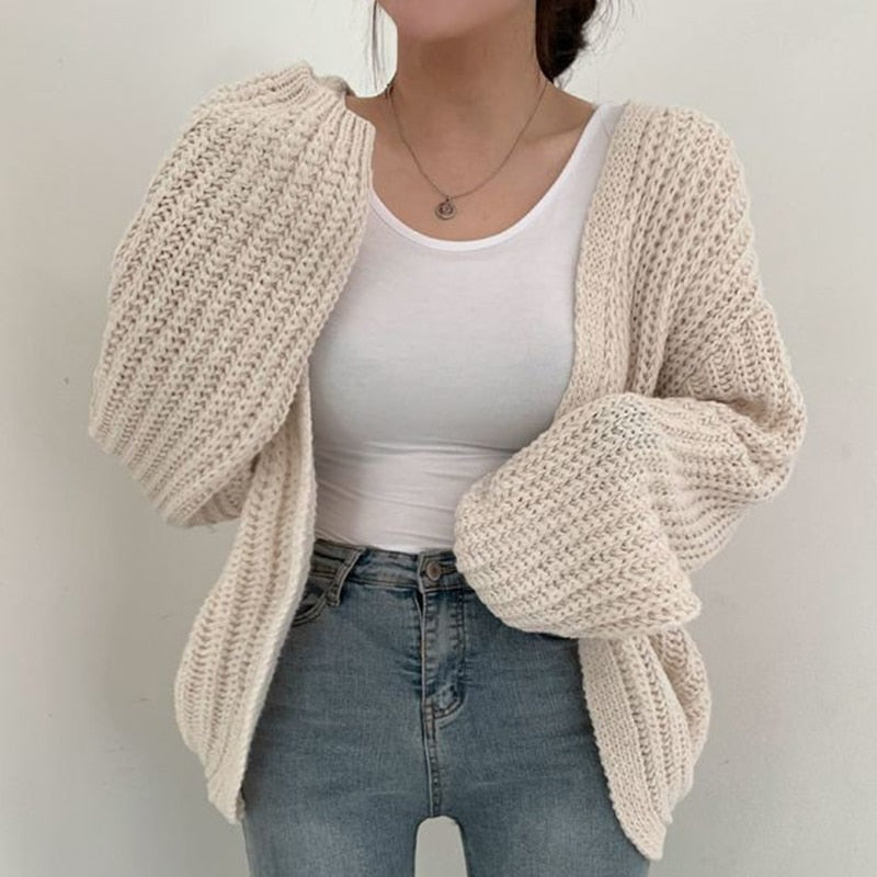 Cream chunky cardigan worn open over a white top and high-waisted jeans, highlighting the textured knit and rounded balloon sleeves.