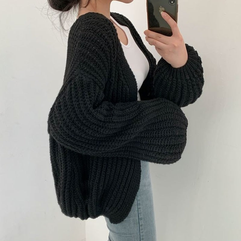 Black open-front cardigan shown from the side with dramatic balloon sleeves and a relaxed silhouette over a white top and jeans.