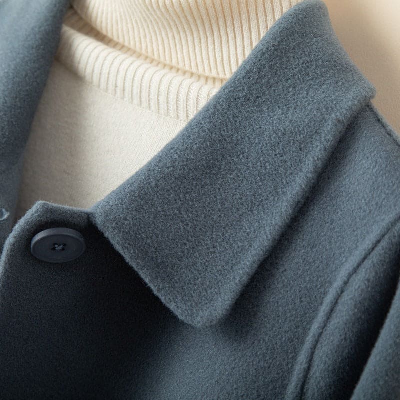 A mid length button front coat with a pointed collar, long sleeves, and side welt pockets shown on a hanger._5