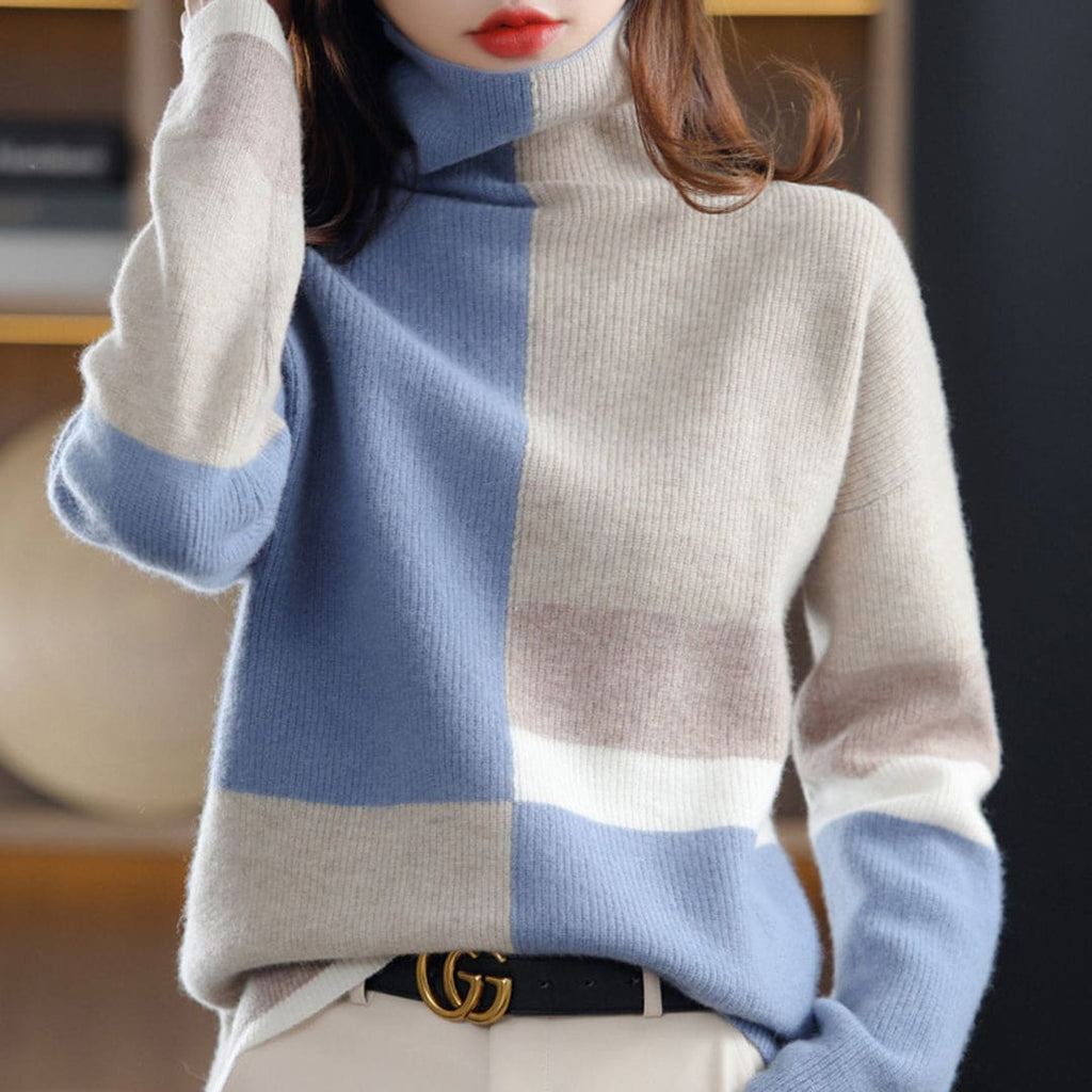 Woman wearing a color block turtleneck sweater with geometric panels in blue and beige tones, paired with black pants and a belt._0
