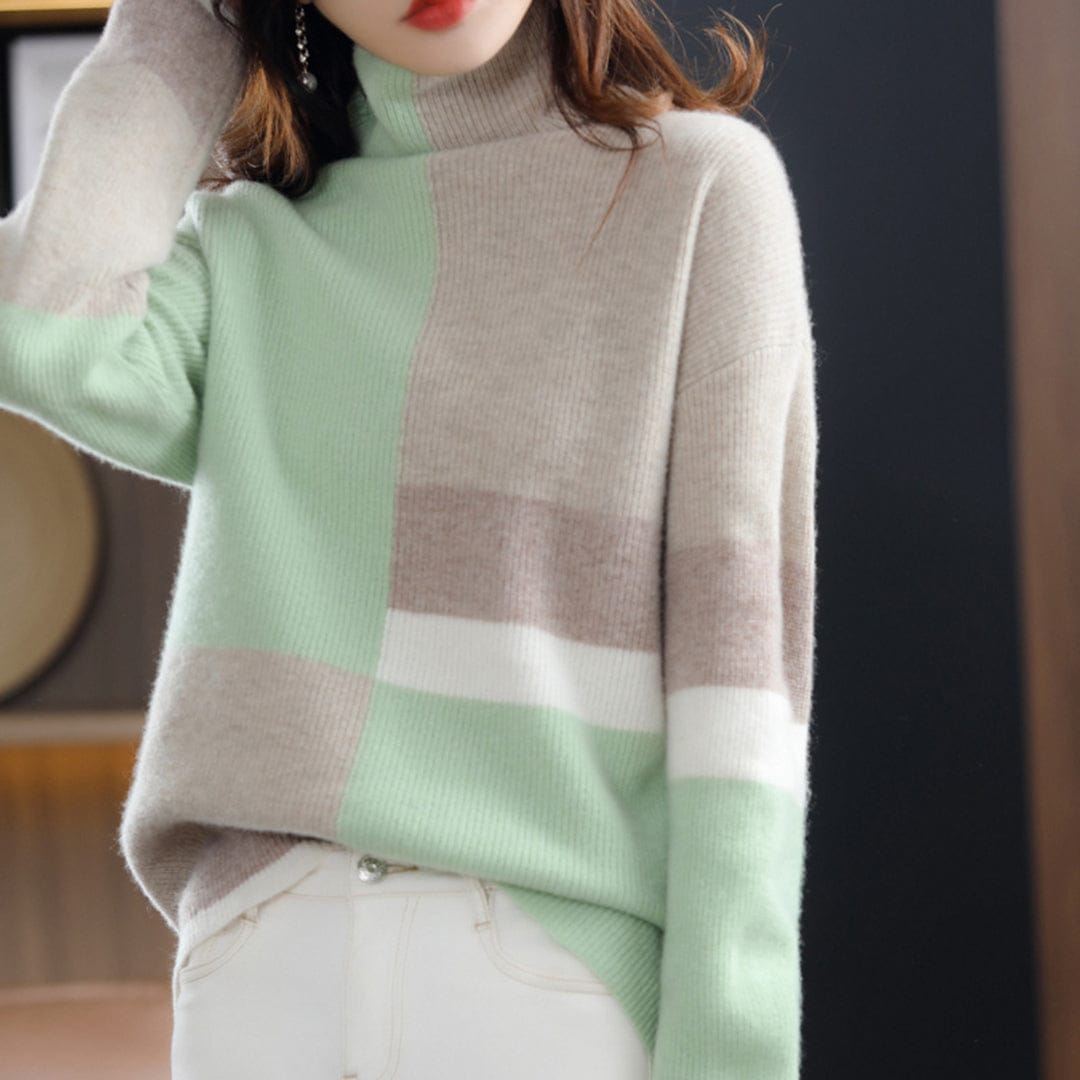 Woman wearing a color block turtleneck sweater with geometric panels in blue and beige tones, paired with black pants and a belt._1