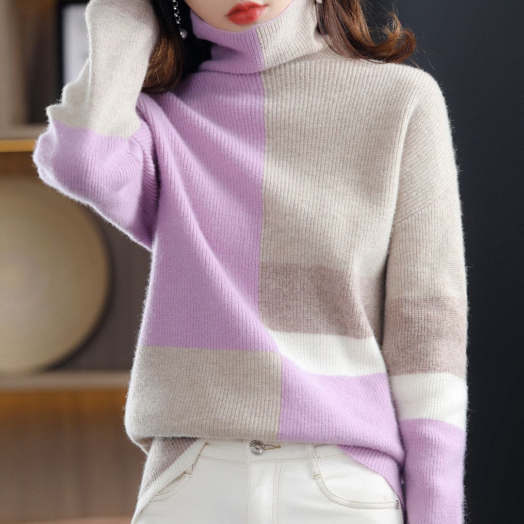 Woman wearing a color block turtleneck sweater with geometric panels in blue and beige tones, paired with black pants and a belt._2