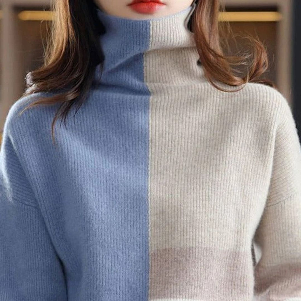 Woman wearing a color block turtleneck sweater with geometric panels in blue and beige tones, paired with black pants and a belt._4