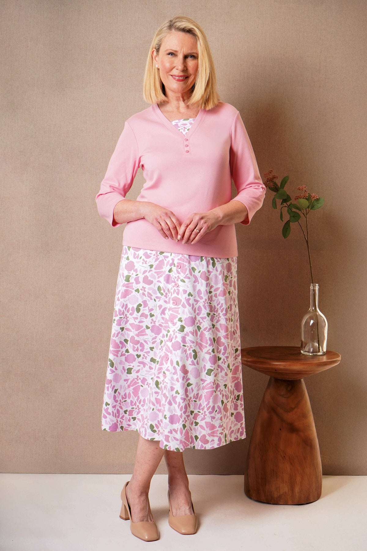 Woman wearing a pink v-neck top with a three-button placket and three-quarter sleeves, with a pink and green floral skirt._2