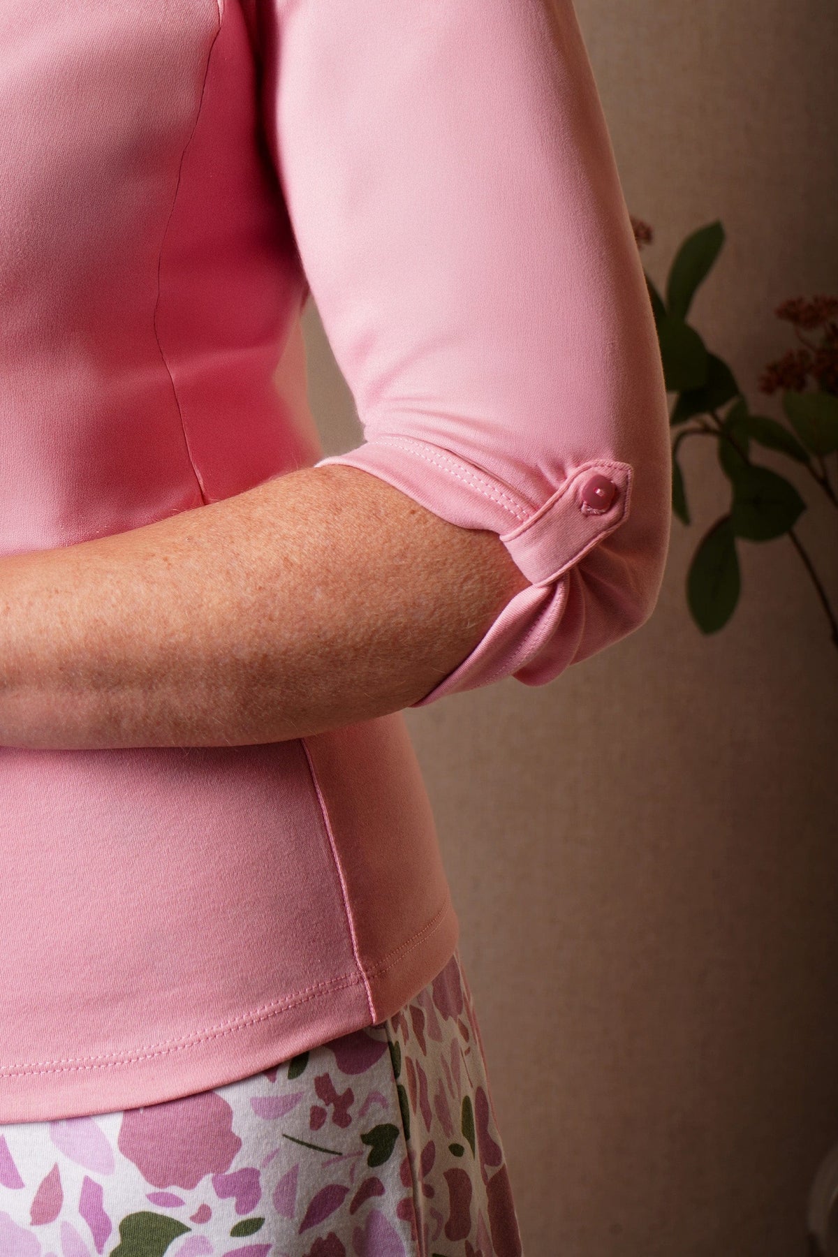 Woman wearing a pink v-neck top with a three-button placket and three-quarter sleeves, with a pink and green floral skirt._3