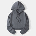 Charcoal gray cropped hoodie laid flat, highlighting the raised hood, long sleeves, ribbed waistband, and dark drawstrings.