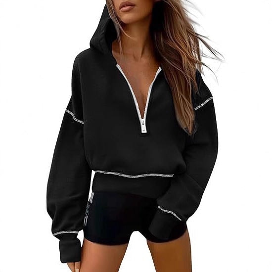 Black cropped hooded half-zip hoodie featuring white contrast stitching and a light zipper against black shorts.