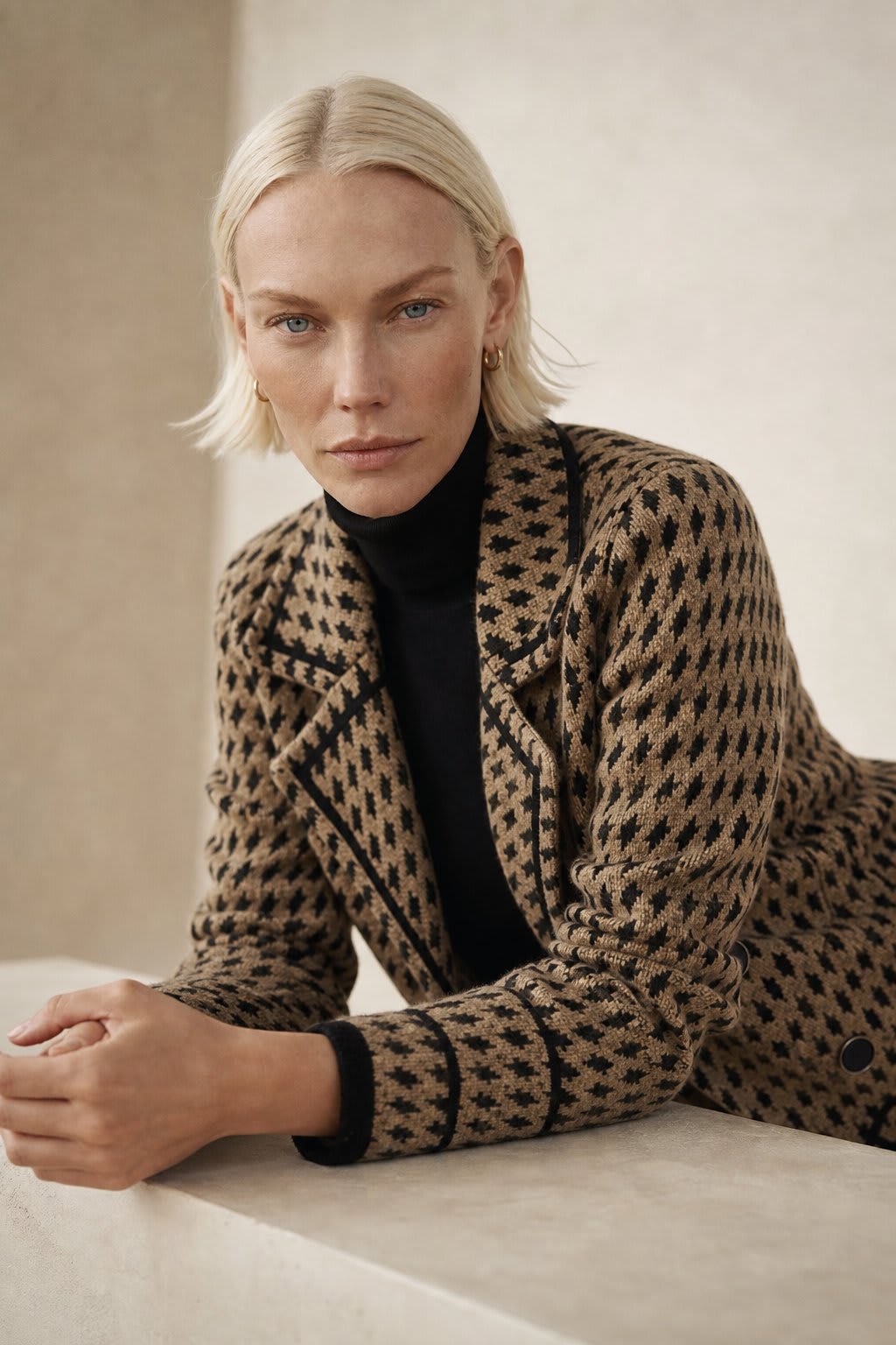 Woman wearing a cropped houndstooth knit jacket with double-breasted buttons over a black turtleneck._0