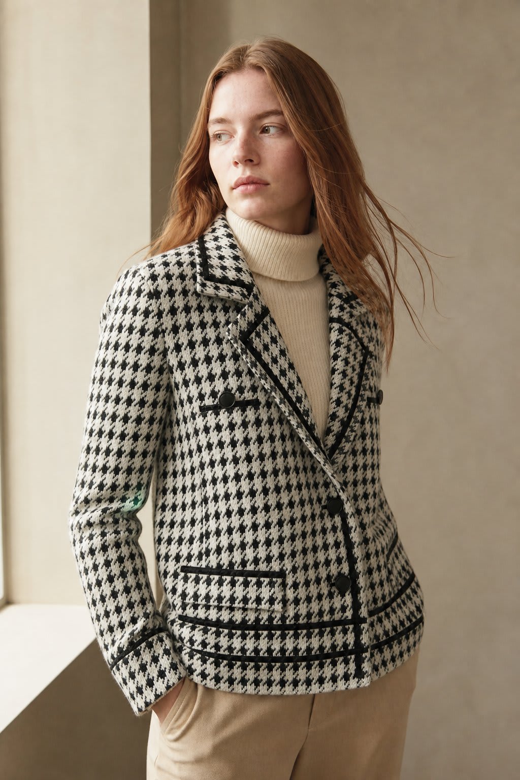 Woman wearing a cropped houndstooth knit jacket with double-breasted buttons over a black turtleneck._2