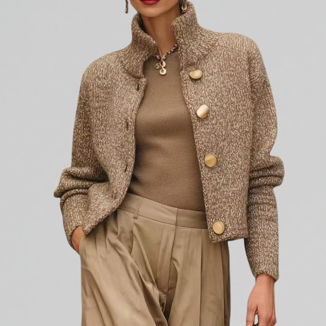 Woman wearing a cropped tailored jacket with oversized gold buttons, styled with a fitted turtleneck and pleated trousers in neutral tones._0