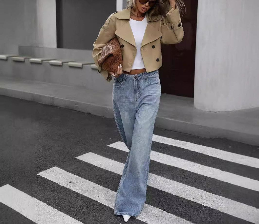 Woman wearing a cropped khaki trench coat with double breasted front, white crop top, and wide leg jeans while crossing the street._0