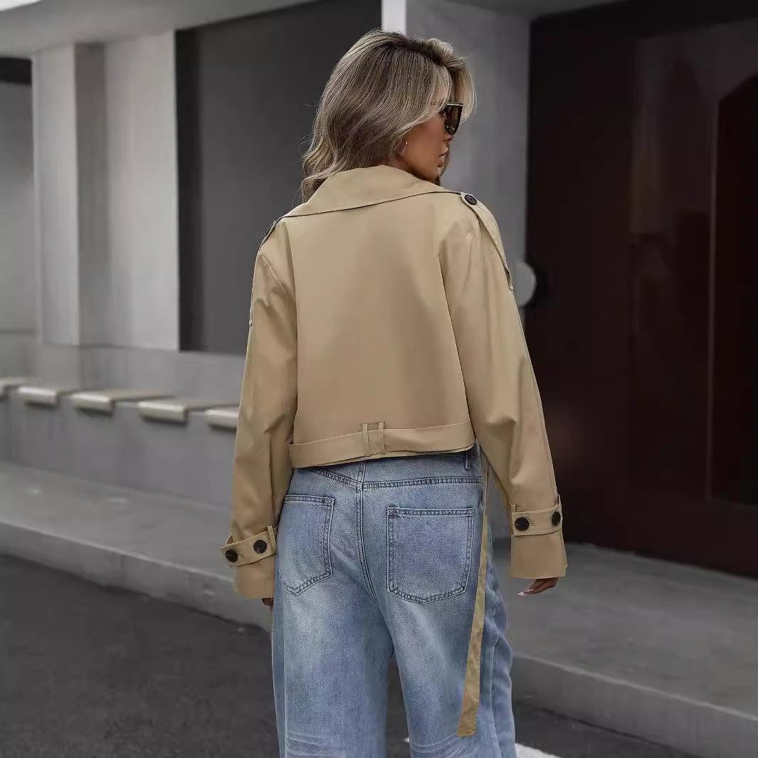 Woman wearing a cropped khaki trench coat with double breasted front, white crop top, and wide leg jeans while crossing the street._1