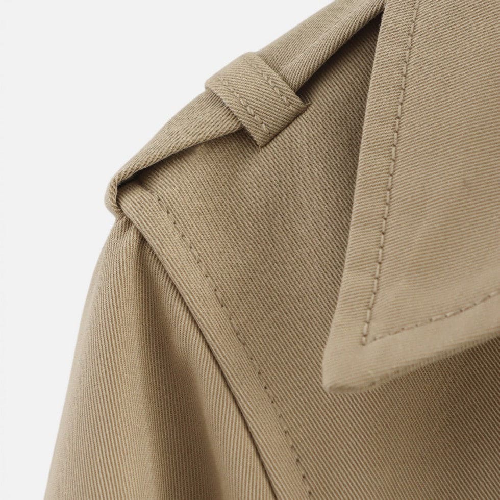 Cropped trench jacket in a neutral tone with double breasted button closure, notched lapel collar, shoulder epaulettes, and belted buckle cuffs displayed flat on a light background._7