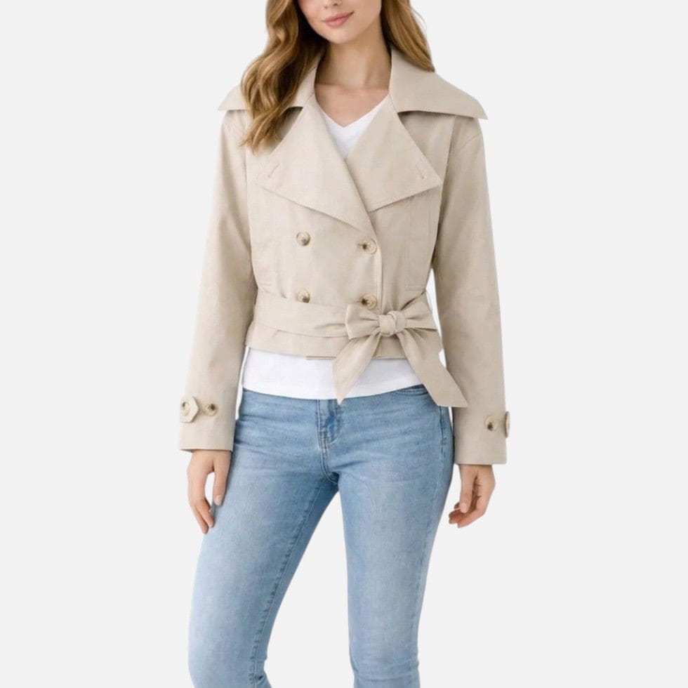 Woman wearing a cropped trench jacket with notch collar, double-breasted buttons, and belted waist styled with a white top and light jeans._0