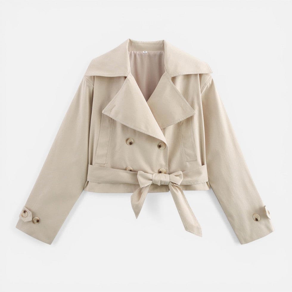 Woman wearing a cropped trench jacket with notch collar, double-breasted buttons, and belted waist styled with a white top and light jeans._1