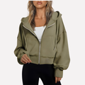 Olive cropped zip-up hoodie with drawstring hood, roomy sleeves, front pockets, and ribbed hem and cuffs, styled over a white top.
