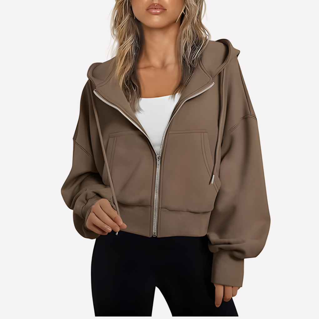 Brown cropped zip-up hoodie styled over a white top, with a drawstring hood, relaxed sleeves, front pockets, and ribbed cuffs.