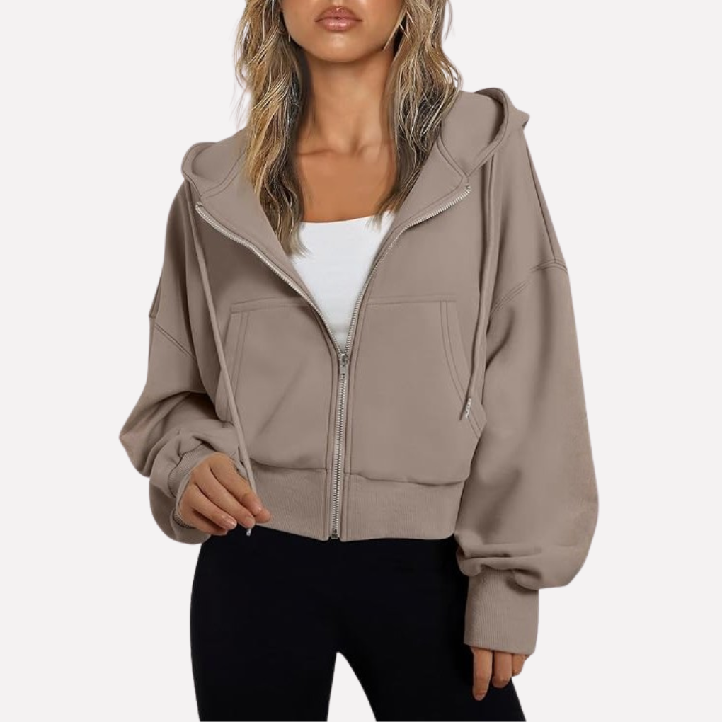 Taupe cropped hoodie shown zipped over a white top, with a drawstring hood, roomy sleeves, and front pockets.