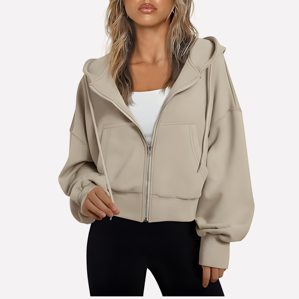 Beige cropped hoodie layered over a white top, showing its drawstring hood, zip front, oversized sleeves, and front pockets.