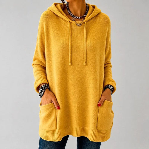 Woman wearing a mustard yellow oversized hooded knit tunic with drawstring hood, ribbed cuffs and two front patch pockets over blue jeans._0