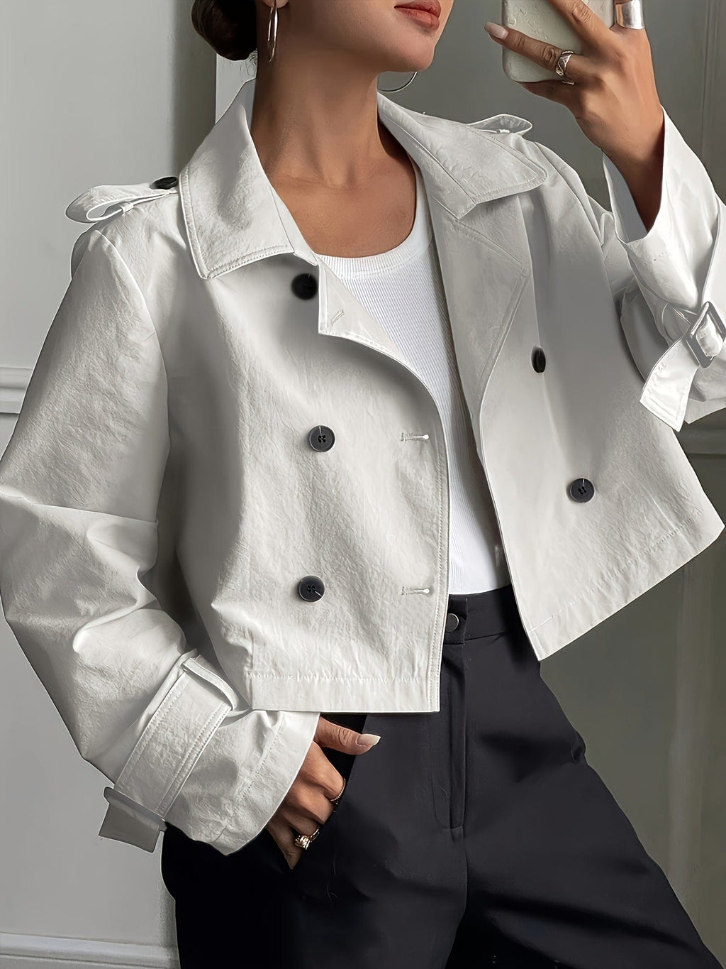 Woman wearing a cropped double-breasted jacket with notch lapel, epaulette shoulder tabs, and buckle cuff sleeves, paired with a white top and dark trousers._0