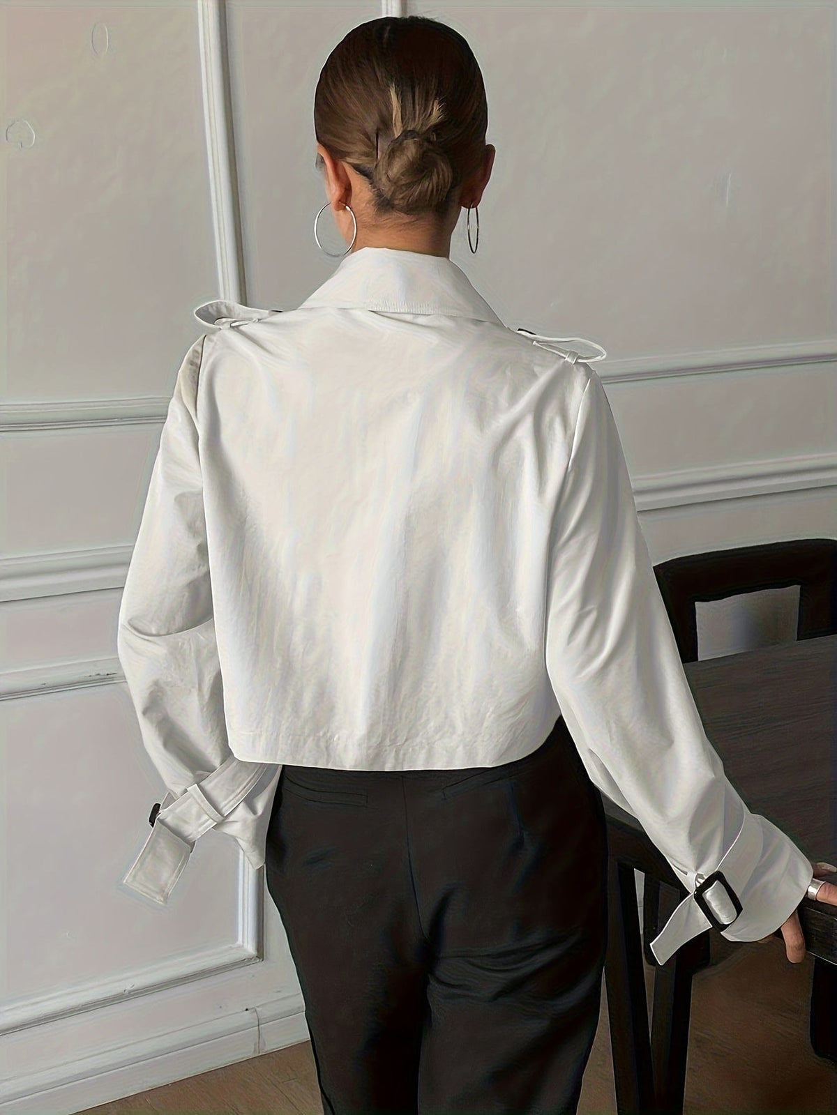 Woman wearing a cropped double-breasted jacket with notch lapel, epaulette shoulder tabs, and buckle cuff sleeves, paired with a white top and dark trousers._2