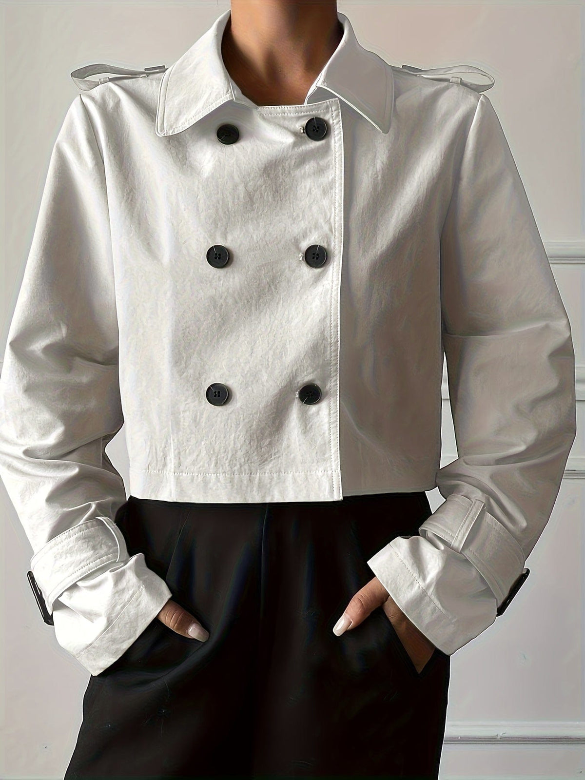 Woman wearing a cropped double-breasted jacket with notch lapel, epaulette shoulder tabs, and buckle cuff sleeves, paired with a white top and dark trousers._3