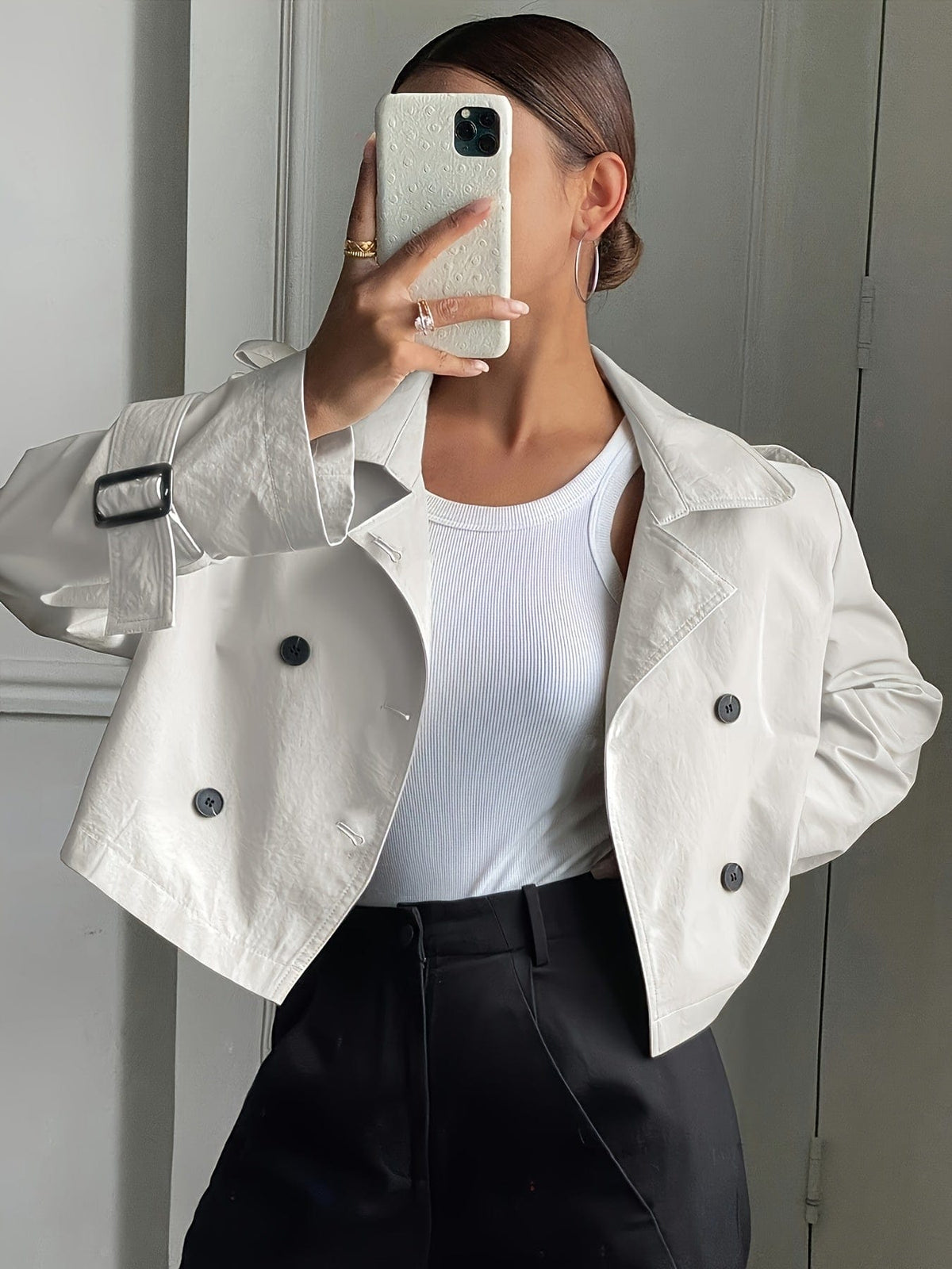 Woman wearing a cropped double-breasted jacket with notch lapel, epaulette shoulder tabs, and buckle cuff sleeves, paired with a white top and dark trousers._4