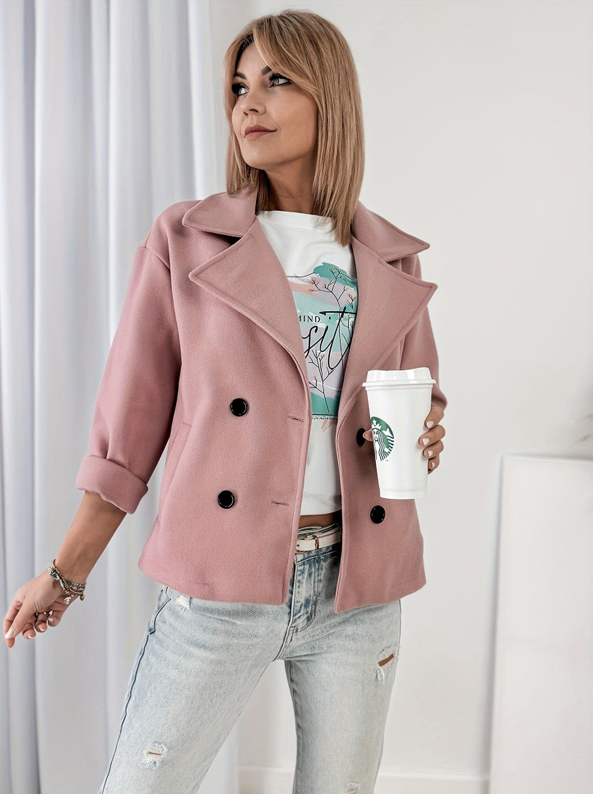 Woman wearing a cropped double breasted pea coat with notched lapel collar and rolled sleeves, styled over a graphic tee and light denim jeans while holding a coffee cup._0