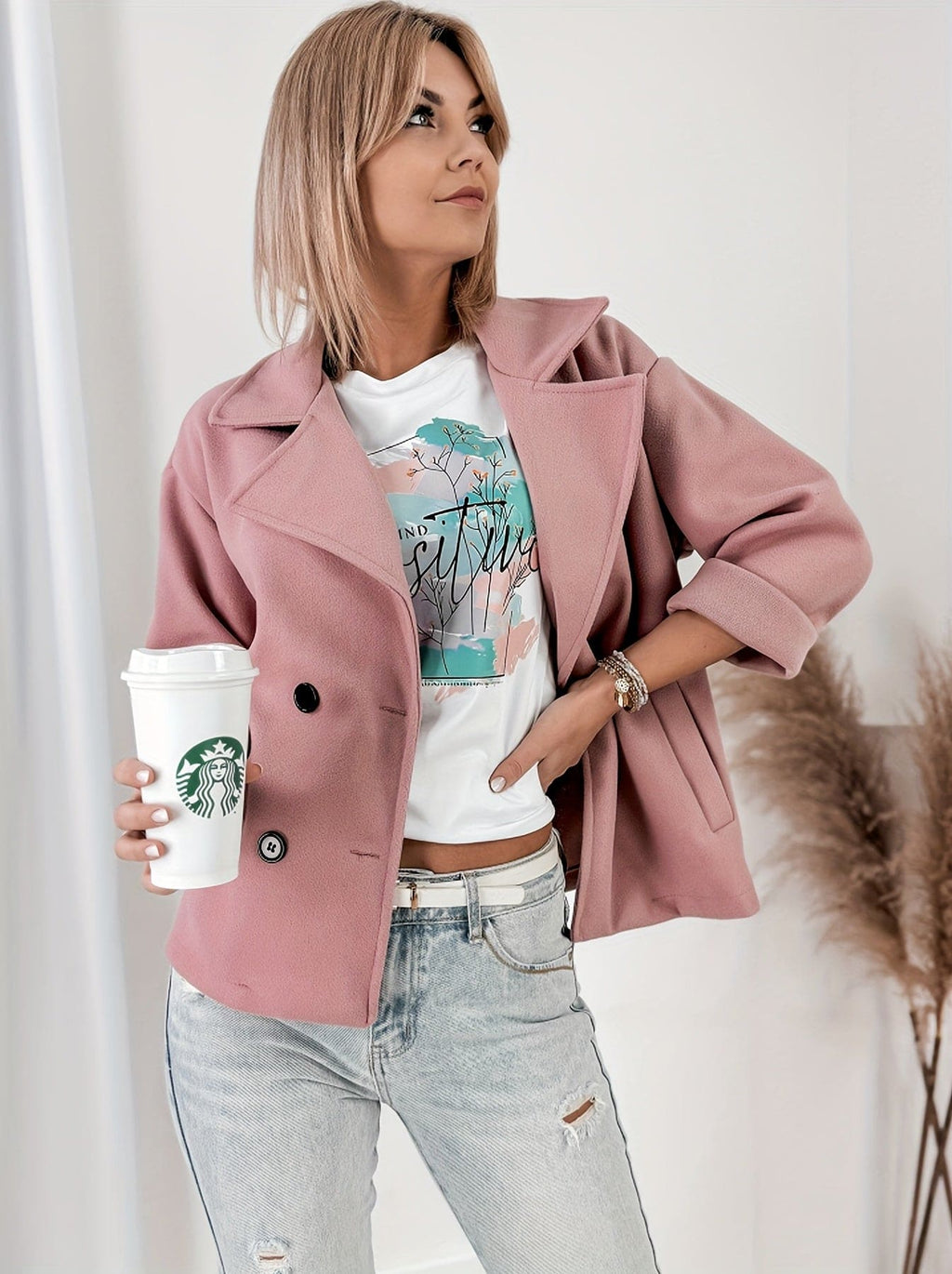 Woman wearing a cropped double breasted pea coat with notched lapel collar and rolled sleeves, styled over a graphic tee and light denim jeans while holding a coffee cup._3