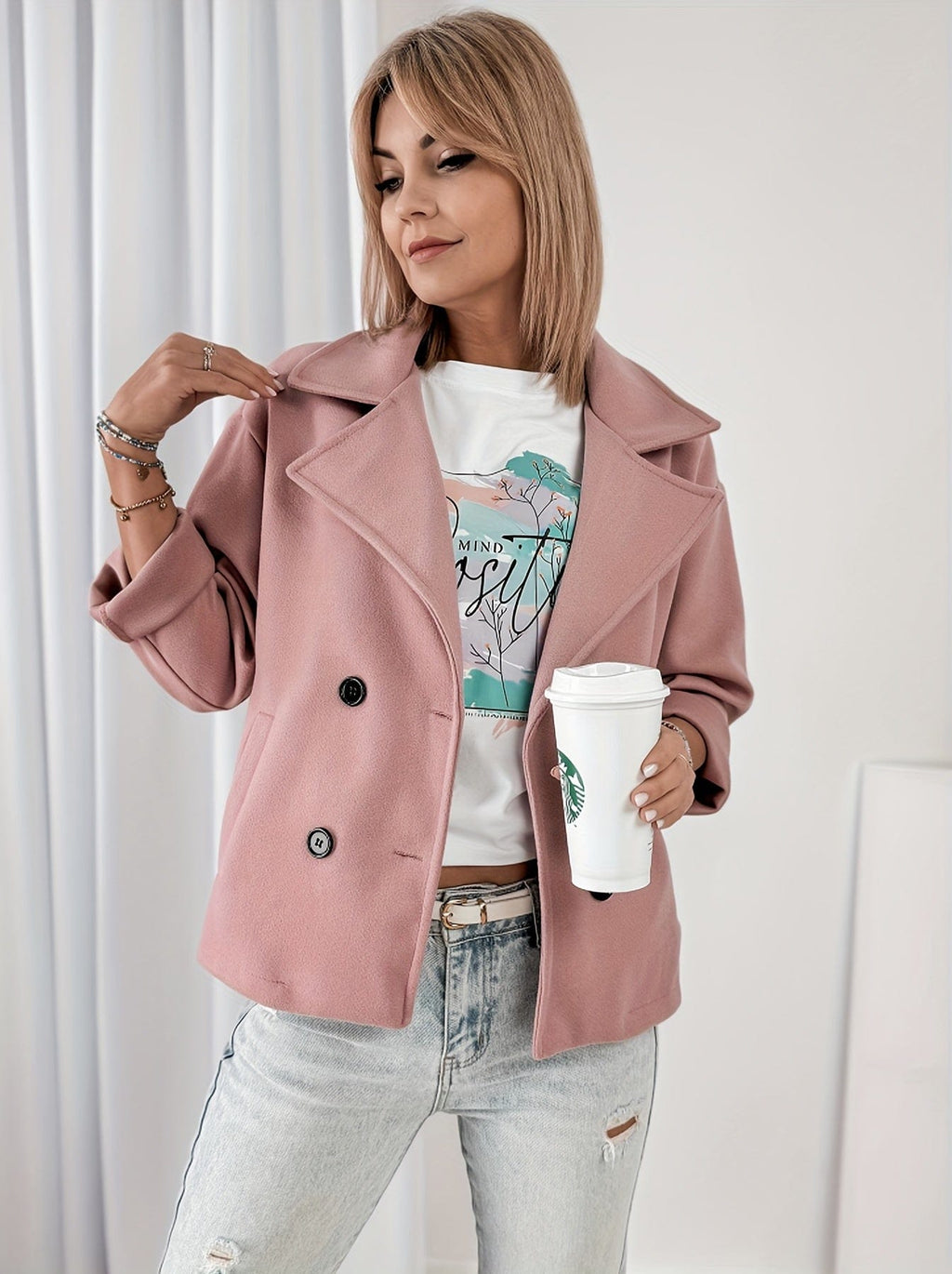 Woman wearing a cropped double breasted pea coat with notched lapel collar and rolled sleeves, styled over a graphic tee and light denim jeans while holding a coffee cup._4