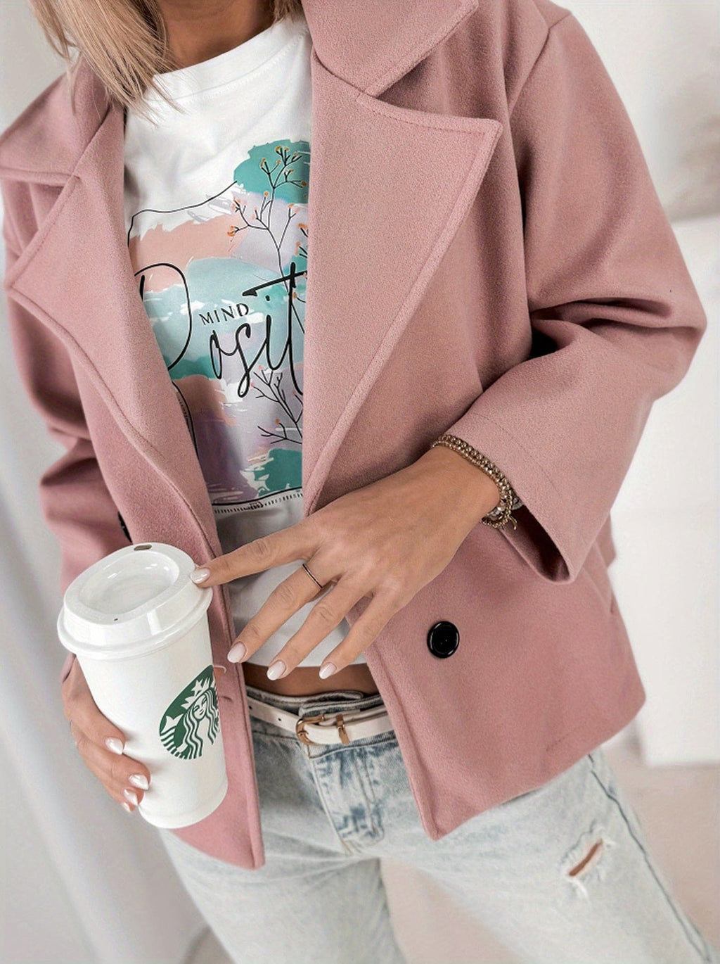 Woman wearing a cropped double breasted pea coat with notched lapel collar and rolled sleeves, styled over a graphic tee and light denim jeans while holding a coffee cup._5