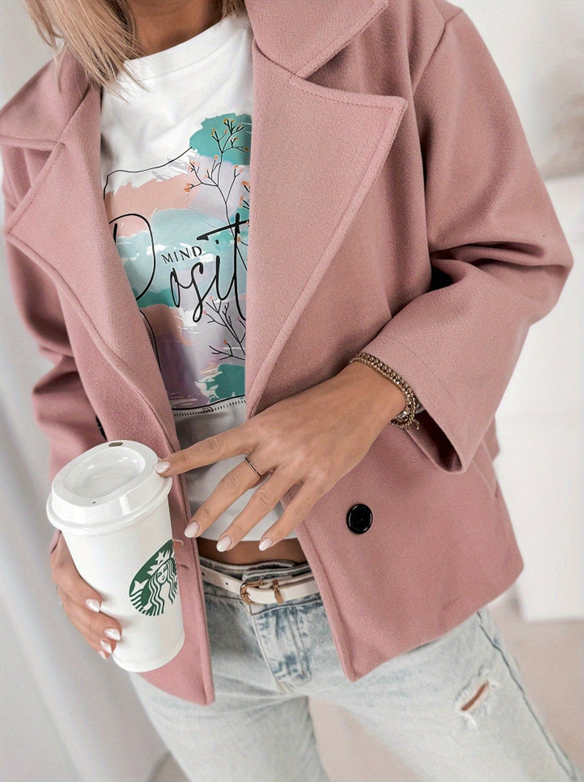 Woman wearing a cropped double breasted pea coat with notched lapel collar and rolled sleeves, styled over a graphic tee and light denim jeans while holding a coffee cup._5