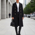 Model wearing a longline double-breasted coat with gold buttons over a white shirt and black pants on a city street._0