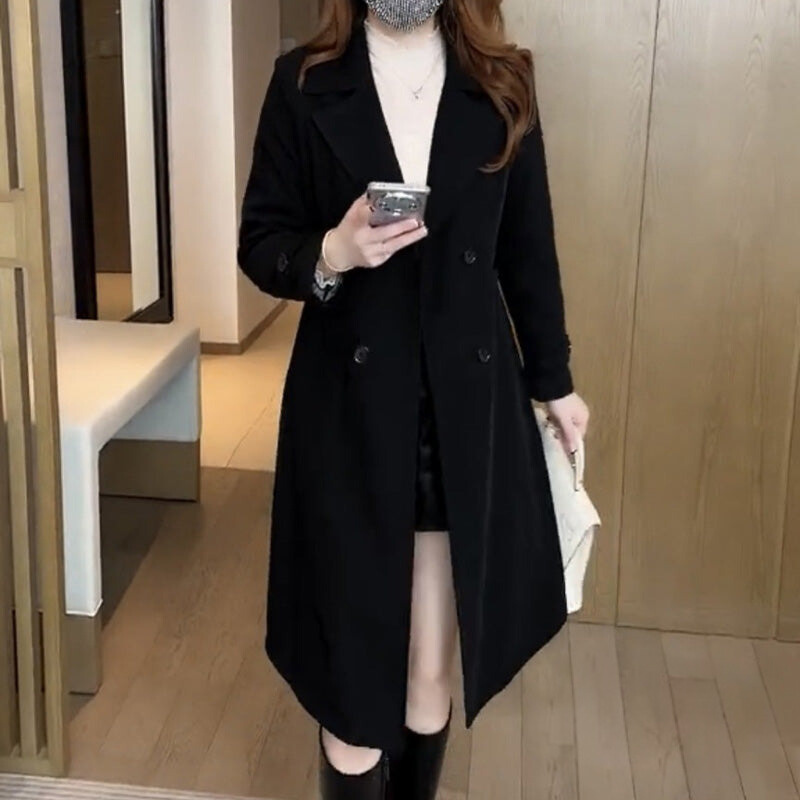 Woman wearing a longline double-breasted trench coat with lapel collar and belted waist in an indoor setting._0