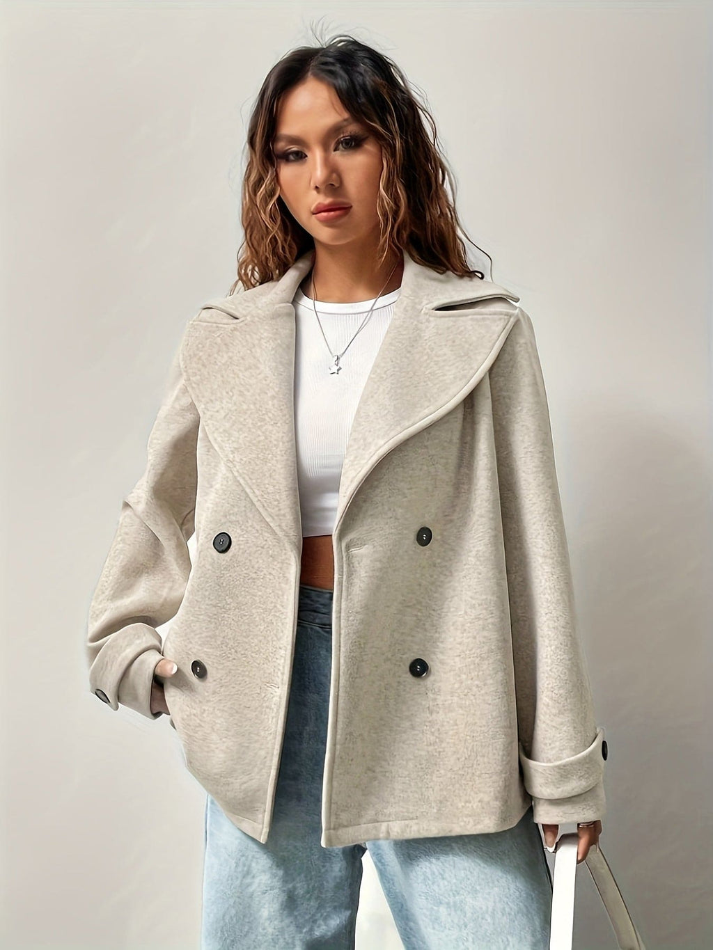 Woman wearing an oversized double-breasted pea coat with notched lapel, white crop top, and light wash jeans against a neutral background._0