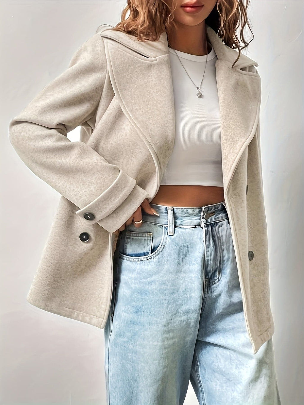 Woman wearing an oversized double-breasted pea coat with notched lapel, white crop top, and light wash jeans against a neutral background._4