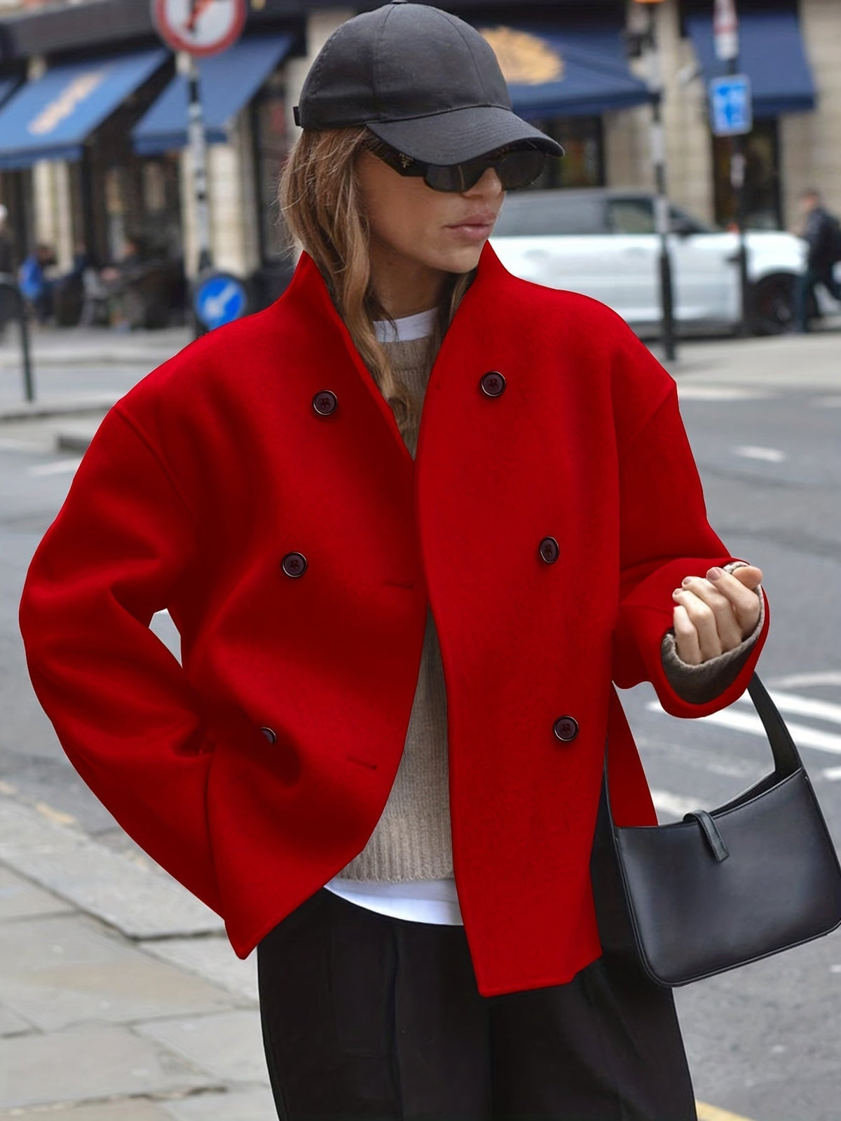 Woman wearing an oversized double breasted pea coat with stand collar and cropped silhouette, styled with a baseball cap on a city street._2