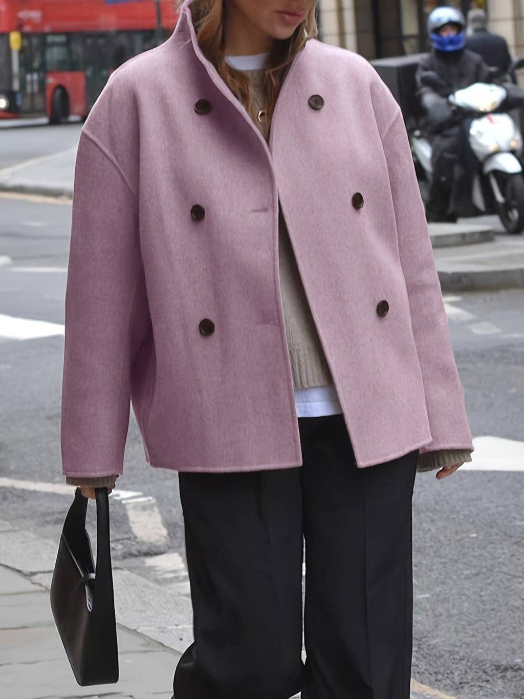 Woman wearing an oversized double breasted pea coat with stand collar and cropped silhouette, styled with a baseball cap on a city street._3